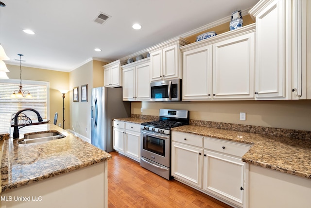 kitchen with white cabinets, sink, appliances with stainless steel finishes, decorative light fixtures, and light hardwood / wood-style floors