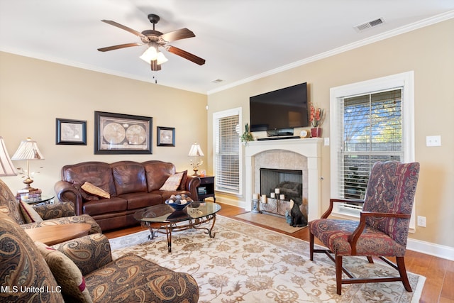 living room featuring ceiling fan, ornamental molding, a fireplace, and light hardwood / wood-style flooring