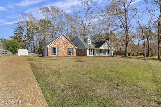 view of front facade with a storage shed, covered porch, an outdoor structure, a front yard, and brick siding