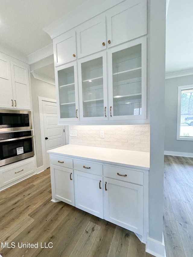 kitchen with light countertops, glass insert cabinets, white cabinets, built in microwave, and oven