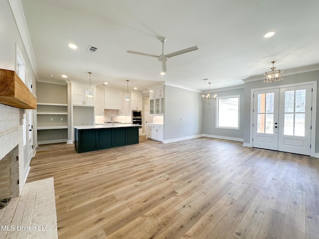 unfurnished living room with light wood-style floors, a brick fireplace, crown molding, and ceiling fan with notable chandelier