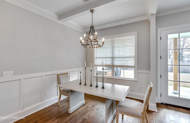 dining area with a wainscoted wall, dark wood-type flooring, an inviting chandelier, a decorative wall, and beam ceiling