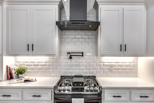 kitchen featuring light countertops, wall chimney range hood, gas range, and white cabinets