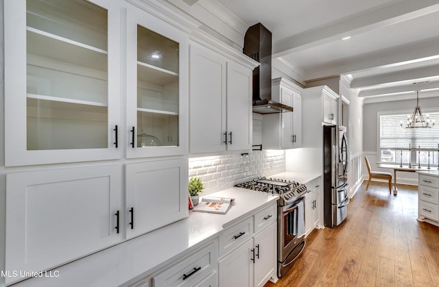 kitchen with stainless steel appliances, white cabinetry, wall chimney range hood, light wood finished floors, and glass insert cabinets