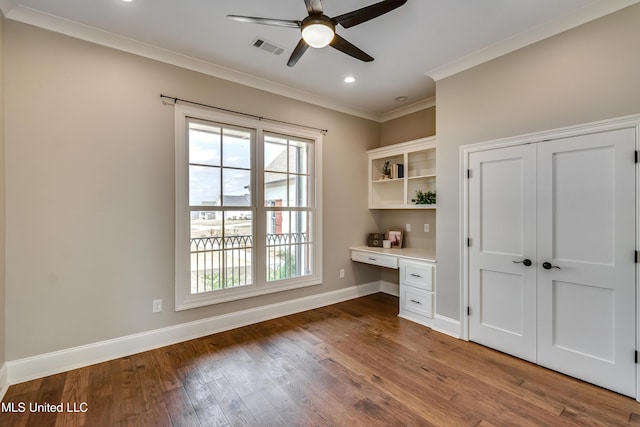 unfurnished office featuring crown molding, built in desk, visible vents, wood finished floors, and baseboards