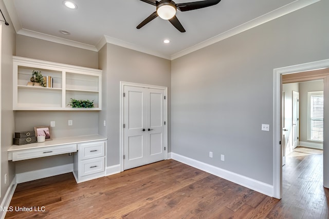 unfurnished office featuring ornamental molding, built in desk, and wood finished floors