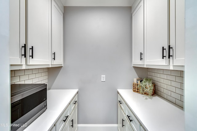 kitchen with stainless steel microwave, backsplash, and white cabinets