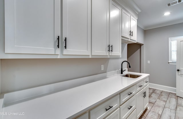 kitchen with baseboards, visible vents, light countertops, white cabinetry, and a sink