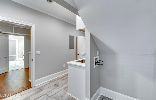 hallway with baseboards, lofted ceiling, electric panel, and light wood-style floors