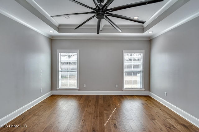 unfurnished room featuring a tray ceiling, hardwood / wood-style floors, and baseboards