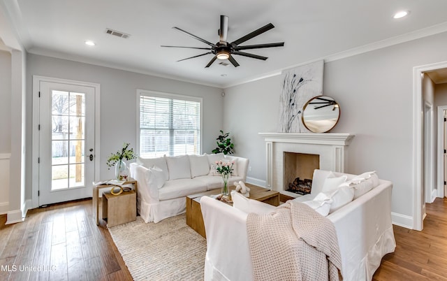 living area with visible vents, a fireplace, ornamental molding, and wood finished floors