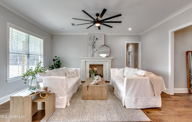 living area with ceiling fan, wood finished floors, visible vents, baseboards, and crown molding