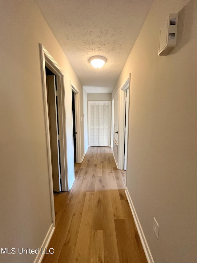 hallway with a textured ceiling and light hardwood / wood-style flooring