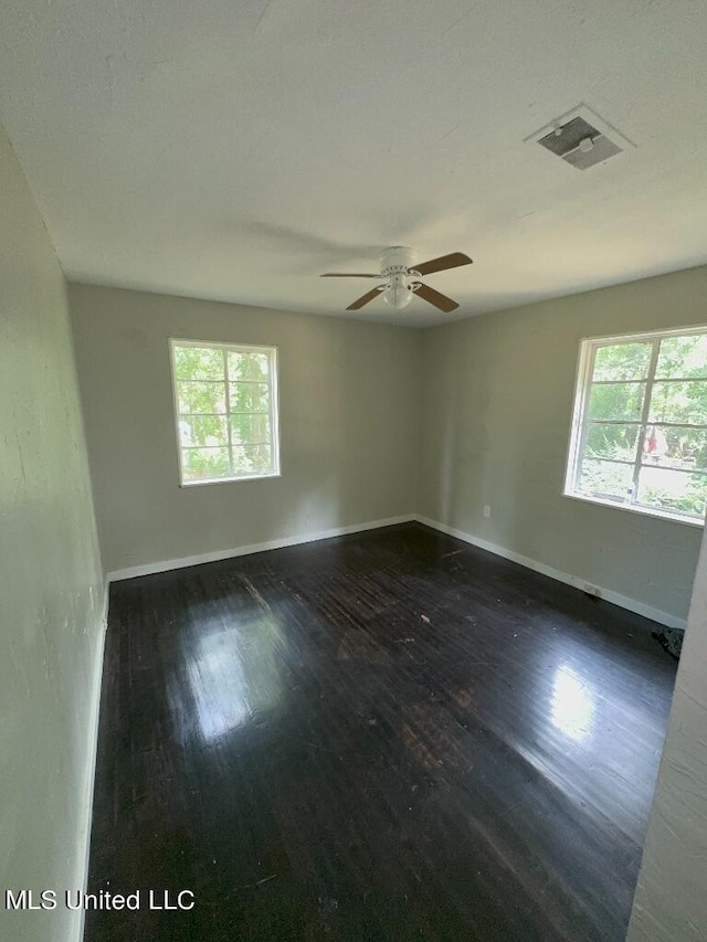 empty room with a wealth of natural light, dark hardwood / wood-style floors, and ceiling fan