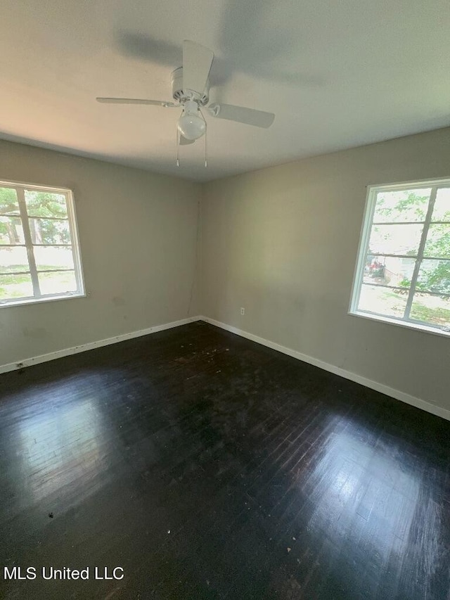 empty room with ceiling fan, a healthy amount of sunlight, and dark hardwood / wood-style flooring