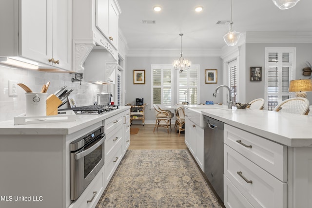 kitchen featuring white cabinetry, light countertops, appliances with stainless steel finishes, backsplash, and crown molding