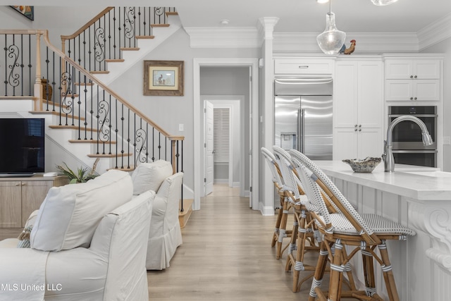 interior space with light wood finished floors, appliances with stainless steel finishes, ornamental molding, white cabinetry, and a kitchen bar