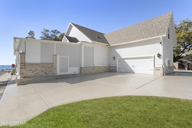 view of side of home featuring a garage, a shingled roof, concrete driveway, and brick siding