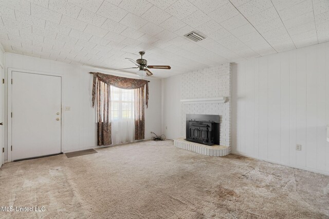 unfurnished living room with a wood stove, ceiling fan, and light colored carpet