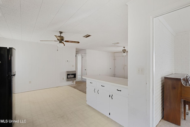 interior space with black refrigerator, ceiling fan, white cabinetry, brick wall, and heating unit