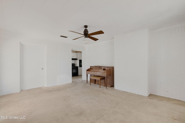 empty room with light carpet, ceiling fan, and brick wall