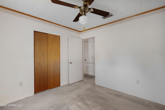 unfurnished bedroom featuring ceiling fan, light colored carpet, crown molding, and a closet