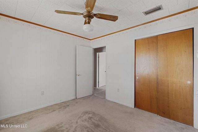 unfurnished bedroom with ceiling fan, a closet, light colored carpet, and ornamental molding