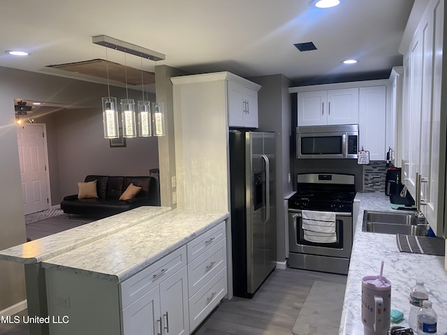 kitchen featuring kitchen peninsula, appliances with stainless steel finishes, white cabinetry, pendant lighting, and light hardwood / wood-style floors