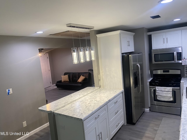 kitchen with appliances with stainless steel finishes, kitchen peninsula, hanging light fixtures, hardwood / wood-style floors, and white cabinets