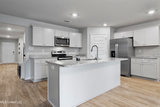 kitchen featuring light hardwood / wood-style flooring, an island with sink, sink, white cabinetry, and appliances with stainless steel finishes