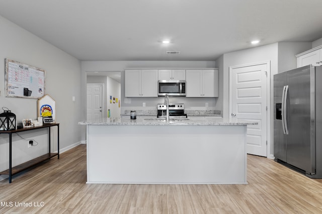 kitchen with white cabinetry, light hardwood / wood-style floors, stainless steel appliances, and a kitchen island with sink