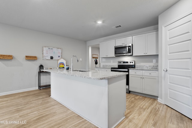 kitchen featuring a center island with sink, sink, white cabinetry, appliances with stainless steel finishes, and light hardwood / wood-style floors