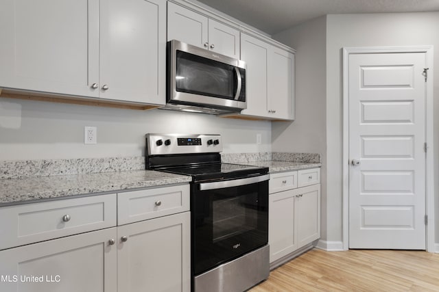 kitchen with light stone countertops, appliances with stainless steel finishes, light wood-type flooring, and white cabinets