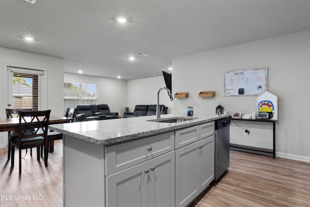 kitchen featuring stainless steel dishwasher, sink, a kitchen island with sink, and light hardwood / wood-style flooring