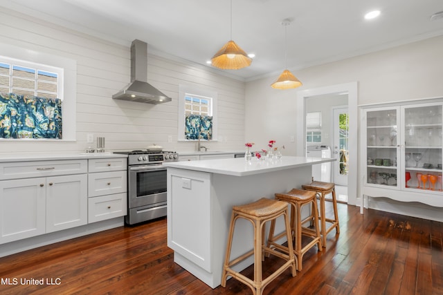 kitchen with a kitchen island, stainless steel range oven, hanging light fixtures, wall chimney exhaust hood, and white cabinets