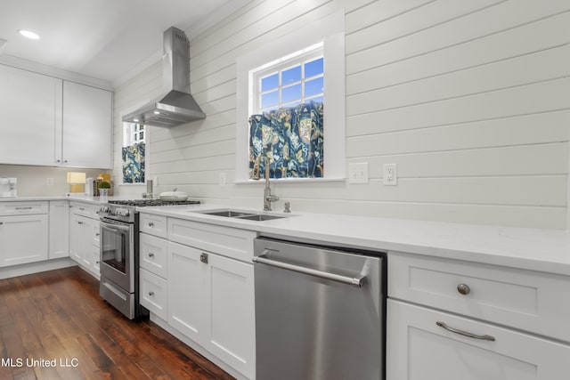 kitchen with wall chimney range hood, dark wood-style flooring, a sink, stainless steel appliances, and white cabinetry