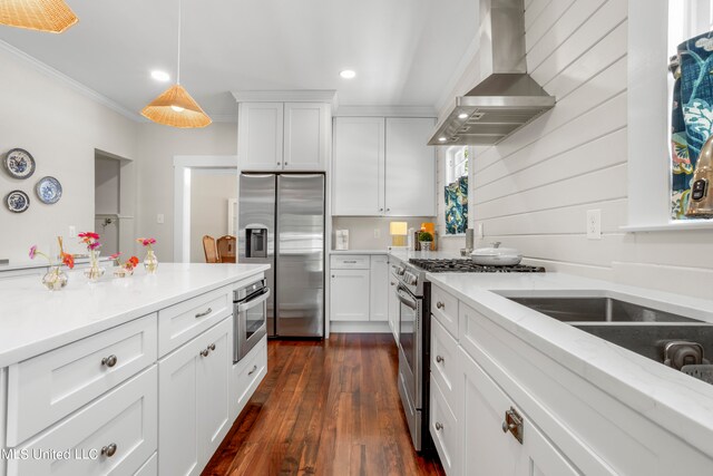 kitchen featuring dark hardwood / wood-style floors, wall chimney exhaust hood, stainless steel appliances, pendant lighting, and white cabinetry