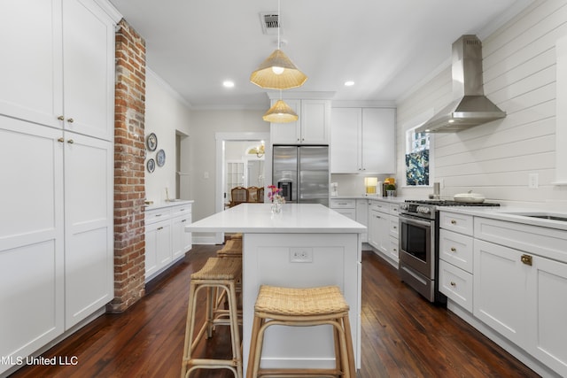 kitchen featuring wall chimney range hood, light countertops, white cabinets, ornamental molding, and stainless steel appliances