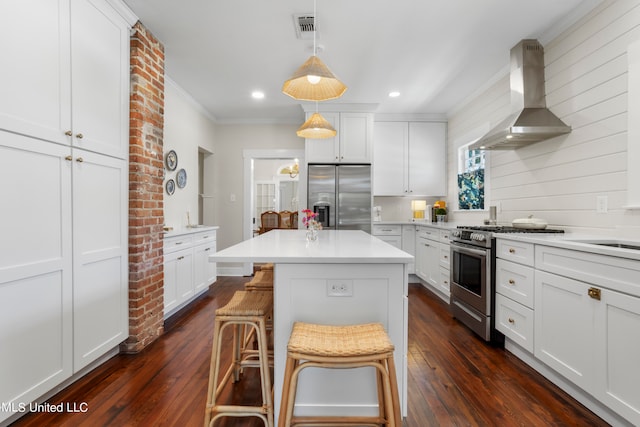 kitchen featuring appliances with stainless steel finishes, decorative light fixtures, range hood, dark wood-type flooring, and a breakfast bar