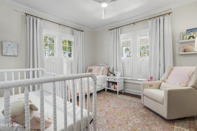 bedroom featuring crown molding, baseboards, wood finished floors, and a crib