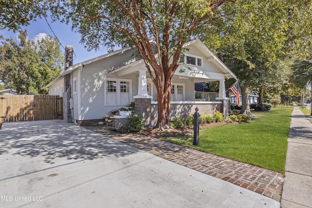bungalow-style house featuring a front yard, fence, covered porch, and a chimney