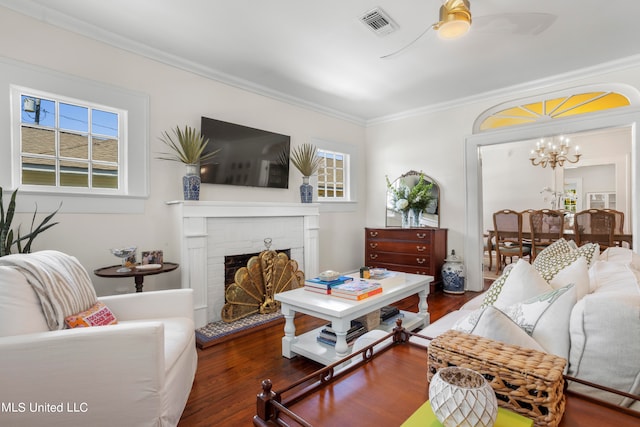 living room featuring crown molding, a brick fireplace, dark hardwood / wood-style floors, and ceiling fan with notable chandelier