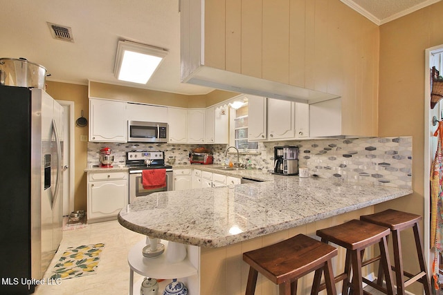 719 Holly Hills Dr, Biloxi, MS 39532 - kitchen with appliances with stainless steel finishes, a peninsula, ornamental molding, white cabinetry, and tasteful backsplash