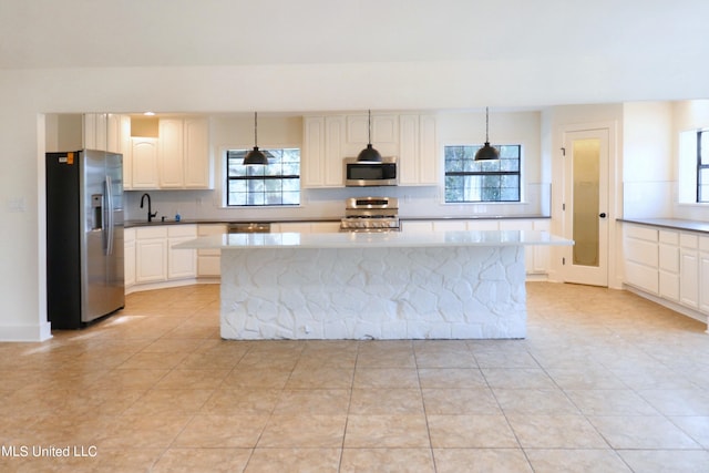 kitchen with light tile patterned flooring, a kitchen island, white cabinetry, stainless steel appliances, and pendant lighting