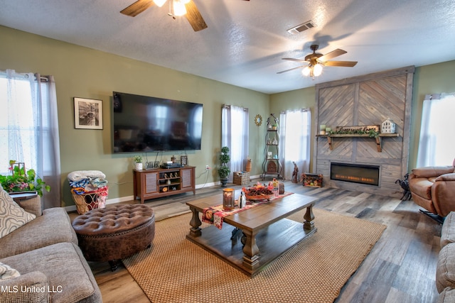 living room with a textured ceiling, a fireplace, wood-type flooring, and ceiling fan