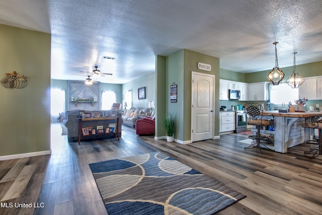 living room with ceiling fan with notable chandelier, dark wood-type flooring, and a textured ceiling