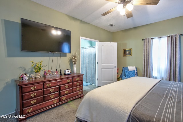 bedroom with a textured ceiling, carpet floors, ceiling fan, and connected bathroom