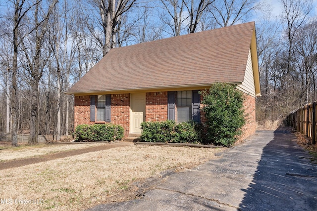 view of front of home with a shingled roof, brick siding, and fence