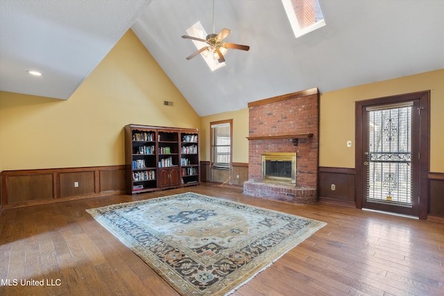 living area featuring a skylight, a fireplace, visible vents, wainscoting, and hardwood / wood-style floors