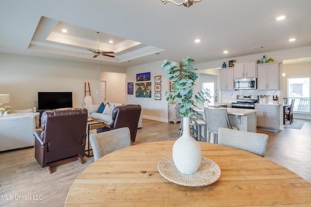 dining space featuring ceiling fan, ornamental molding, a tray ceiling, and light wood-type flooring